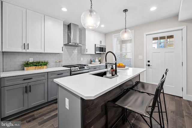 kitchen featuring dark wood finished floors, gray cabinets, appliances with stainless steel finishes, a sink, and wall chimney exhaust hood