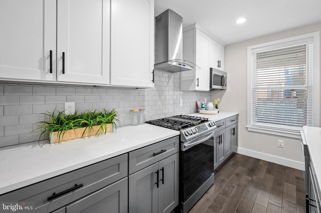 kitchen featuring wall chimney exhaust hood, stainless steel appliances, dark wood finished floors, and gray cabinetry