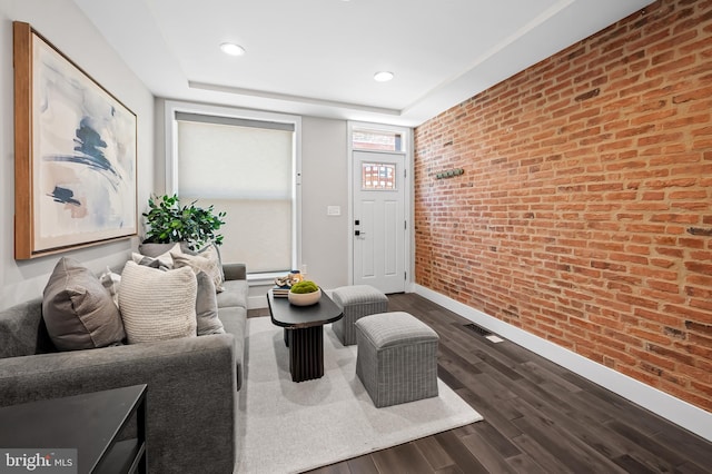 living area with dark wood-style floors, brick wall, baseboards, and recessed lighting