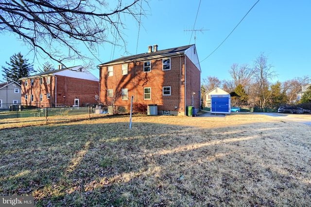 back of property featuring fence, brick siding, and a yard