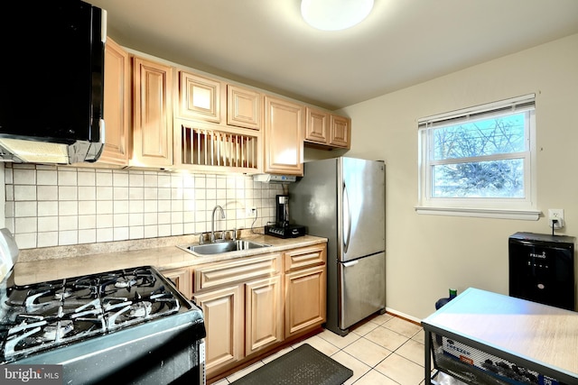 kitchen featuring tasteful backsplash, light countertops, gas range oven, freestanding refrigerator, and a sink