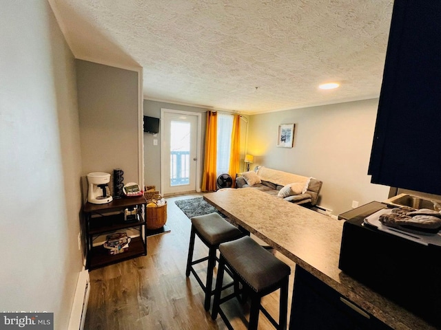 kitchen featuring hardwood / wood-style flooring, a baseboard radiator, a textured ceiling, and a kitchen bar