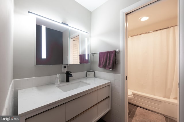 bathroom featuring a wainscoted wall, tile walls, toilet, and vanity