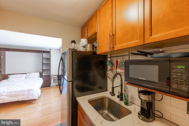 kitchen featuring black microwave, a sink, light wood-style floors, freestanding refrigerator, and brown cabinetry