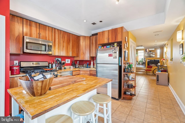 kitchen featuring visible vents, butcher block countertops, appliances with stainless steel finishes, a kitchen breakfast bar, and light tile patterned flooring