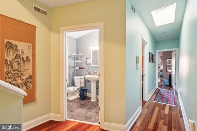 hallway featuring a sink, a skylight, visible vents, and wood finished floors