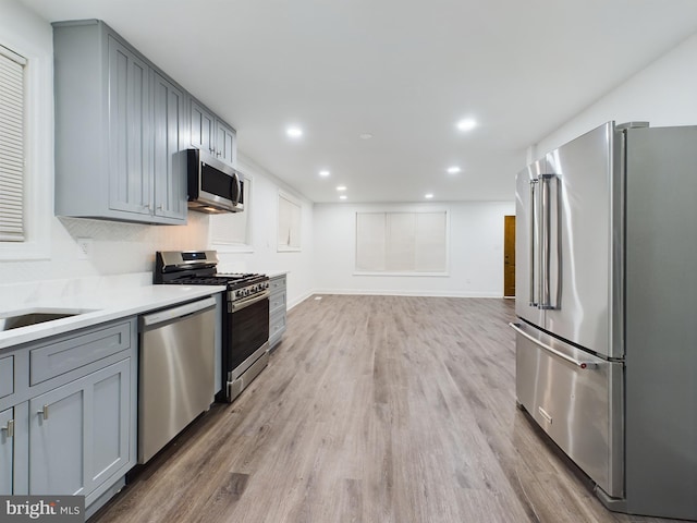 kitchen with stainless steel appliances, gray cabinets, and light wood-type flooring