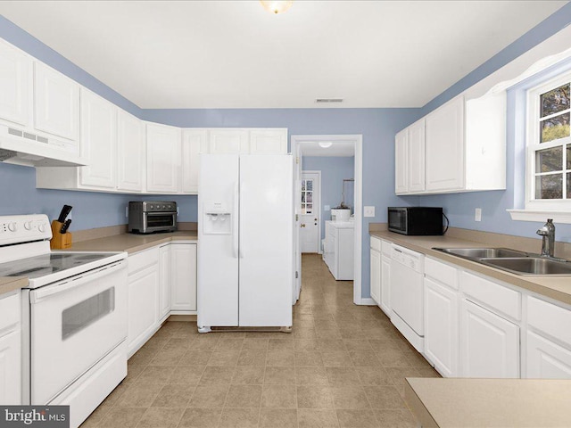 kitchen featuring washing machine and clothes dryer, white cabinetry, a sink, white appliances, and under cabinet range hood