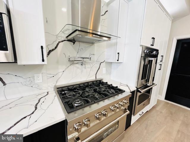 kitchen featuring light stone counters, appliances with stainless steel finishes, island exhaust hood, and white cabinetry