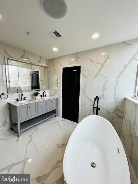 bathroom featuring marble finish floor, visible vents, a sink, and stone wall