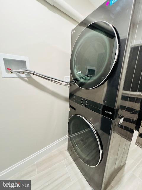 laundry room with baseboards and stacked washer / drying machine