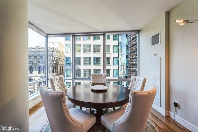 dining area featuring a view of city, dark wood-style flooring, visible vents, baseboards, and expansive windows