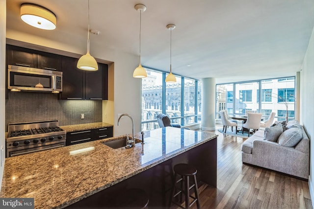 kitchen featuring light stone counters, pendant lighting, stainless steel appliances, open floor plan, and a sink