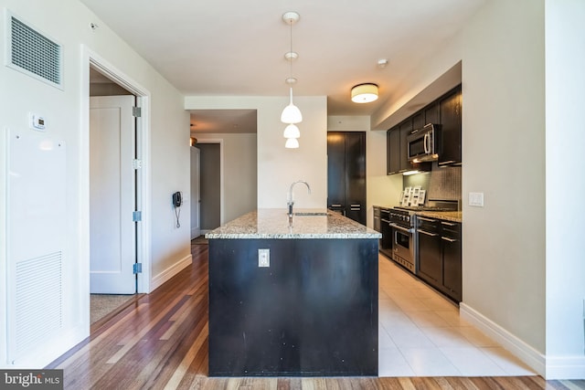 kitchen with pendant lighting, a center island with sink, visible vents, appliances with stainless steel finishes, and light stone countertops