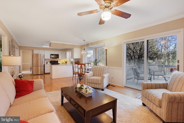 living room featuring ornamental molding, light wood-type flooring, wainscoting, and ceiling fan with notable chandelier