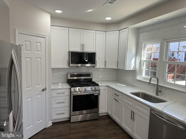 kitchen with appliances with stainless steel finishes, sink, light stone countertops, and white cabinets