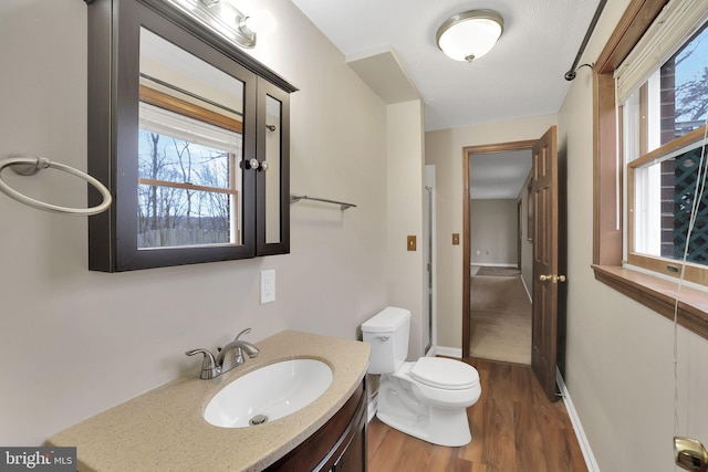 bathroom with toilet, wood finished floors, vanity, and baseboards