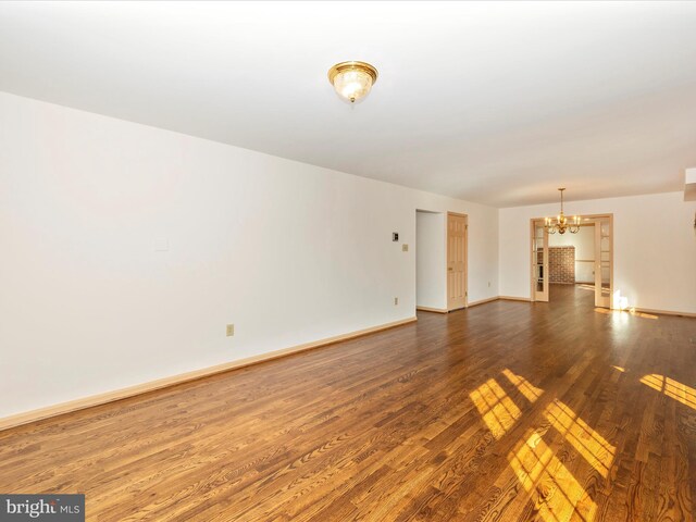 unfurnished room with a notable chandelier, baseboards, and dark wood-style flooring