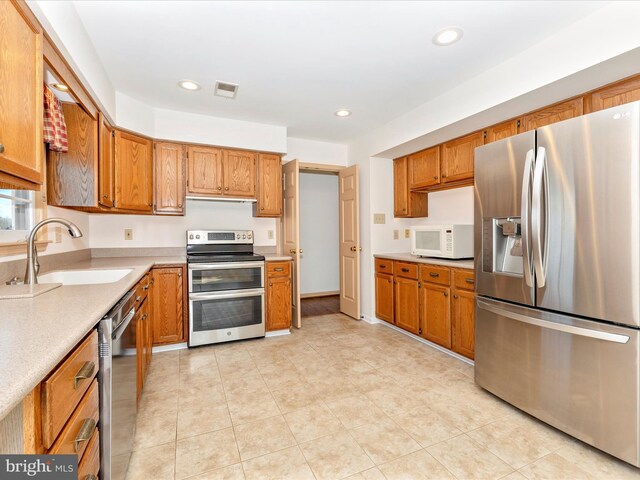 kitchen with visible vents, brown cabinets, stainless steel appliances, light countertops, and a sink