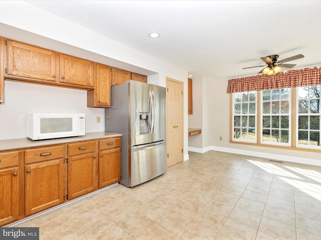 kitchen featuring brown cabinetry, light countertops, stainless steel fridge with ice dispenser, and white microwave