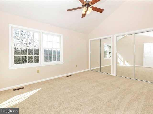 unfurnished bedroom featuring lofted ceiling, light carpet, two closets, and visible vents