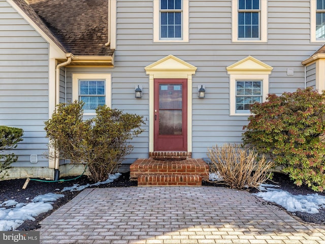 snow covered property entrance with a patio and roof with shingles