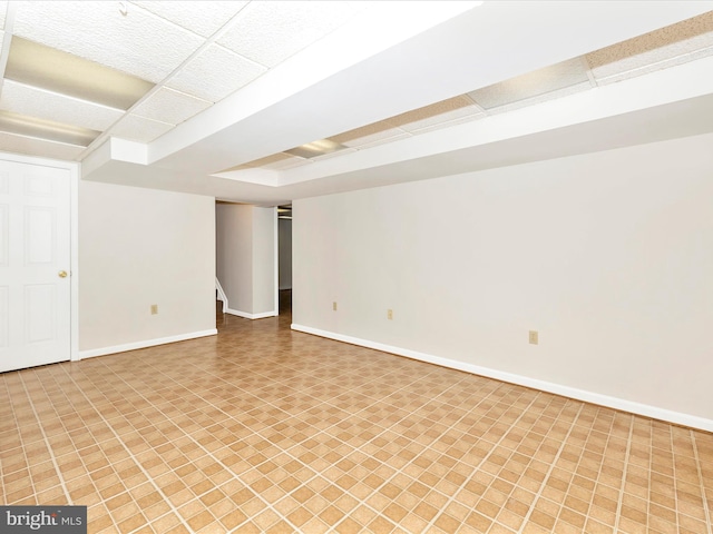 finished below grade area with a paneled ceiling, baseboards, and stairs