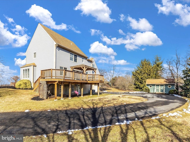 exterior space with driveway, an outdoor structure, a lawn, and a wooden deck