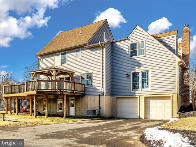 back of house featuring a garage, driveway, central AC unit, a chimney, and a wooden deck