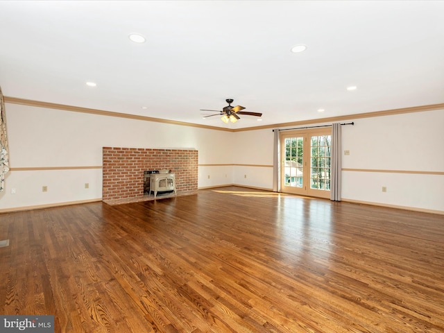 unfurnished living room featuring a wood stove, baseboards, ornamental molding, and wood finished floors