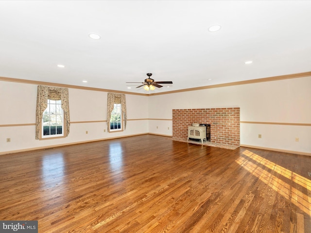 unfurnished living room with a wood stove, crown molding, baseboards, and wood finished floors