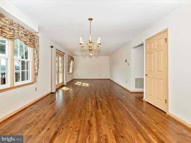 interior space with a chandelier, wood finished floors, visible vents, and baseboards