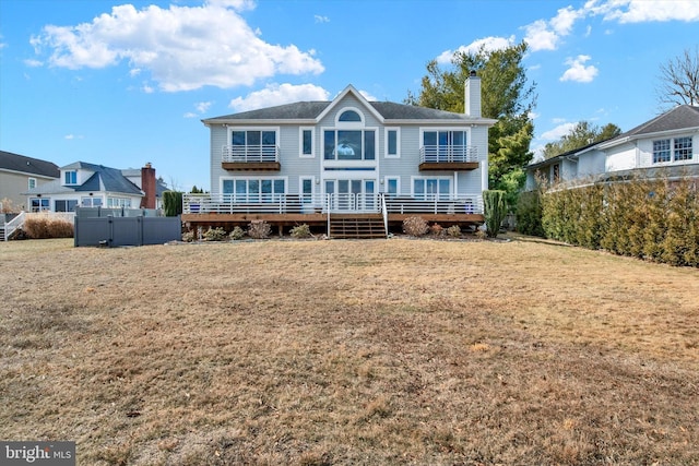 back of house with a lawn, a chimney, and a balcony