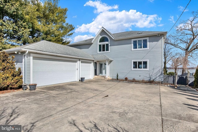 traditional home with an attached garage, driveway, fence, and roof with shingles