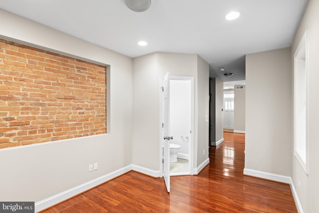 empty room featuring wood-type flooring and brick wall