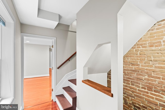 stairway with wood-type flooring and brick wall