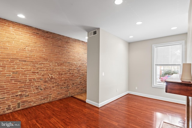 spare room featuring wood-type flooring and brick wall