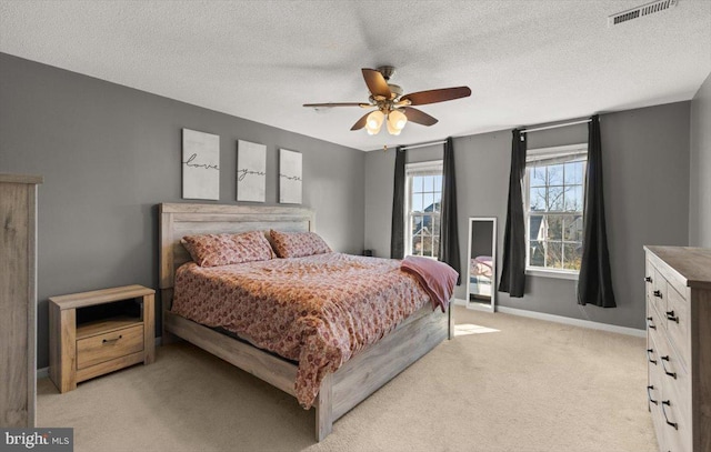 bedroom featuring a textured ceiling, light colored carpet, a ceiling fan, baseboards, and visible vents