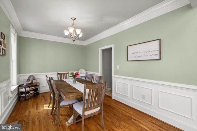 dining room with a wainscoted wall, ornamental molding, dark wood-style flooring, and a notable chandelier