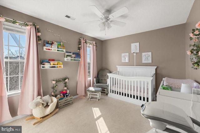 carpeted bedroom with a ceiling fan, a nursery area, and visible vents