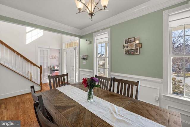 dining space with a chandelier, wood finished floors, stairway, wainscoting, and crown molding