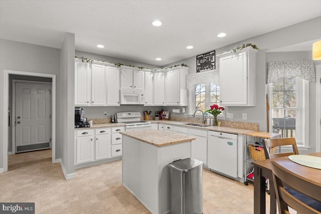 kitchen with recessed lighting, white appliances, a sink, a kitchen island, and white cabinets