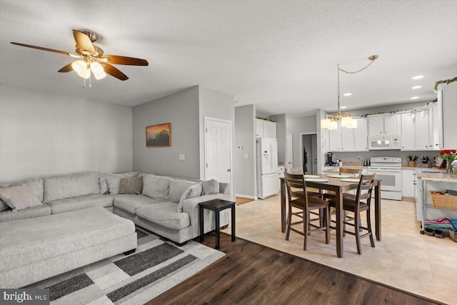 living room with light wood-type flooring, ceiling fan, and a textured ceiling