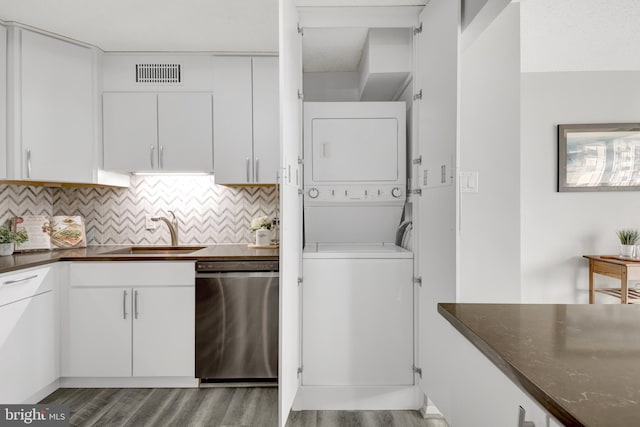 kitchen featuring stacked washer / dryer, sink, white cabinetry, dark stone counters, and stainless steel dishwasher