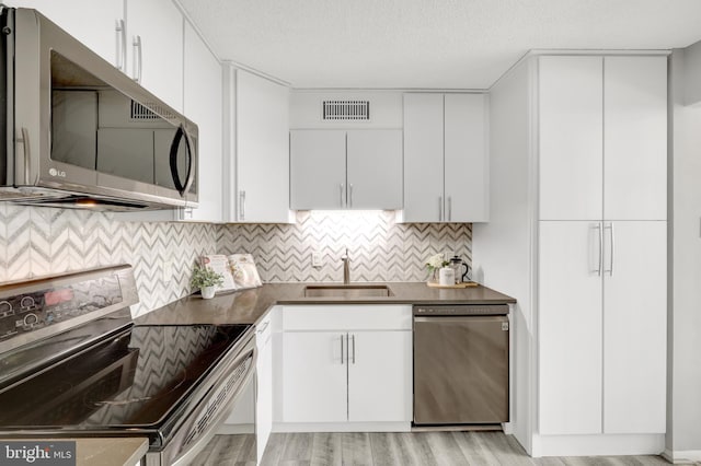 kitchen with appliances with stainless steel finishes, sink, light wood-type flooring, white cabinets, and tasteful backsplash