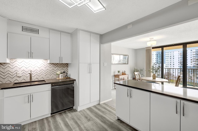 kitchen featuring tasteful backsplash, dishwasher, white cabinets, light hardwood / wood-style floors, and sink