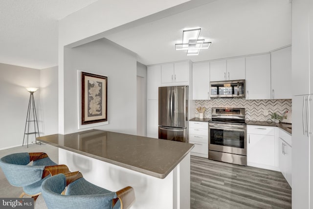 kitchen with white cabinetry, tasteful backsplash, dark wood-type flooring, appliances with stainless steel finishes, and a kitchen breakfast bar