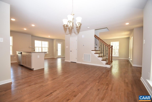 unfurnished living room featuring a healthy amount of sunlight, dark hardwood / wood-style floors, sink, and a notable chandelier