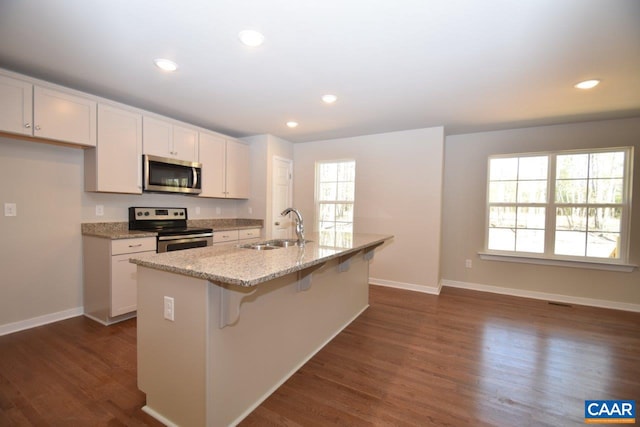 kitchen featuring sink, a center island with sink, stainless steel appliances, white cabinets, and a kitchen bar