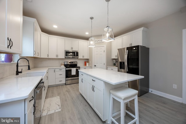 kitchen featuring white cabinetry, decorative light fixtures, a kitchen island, sink, and appliances with stainless steel finishes